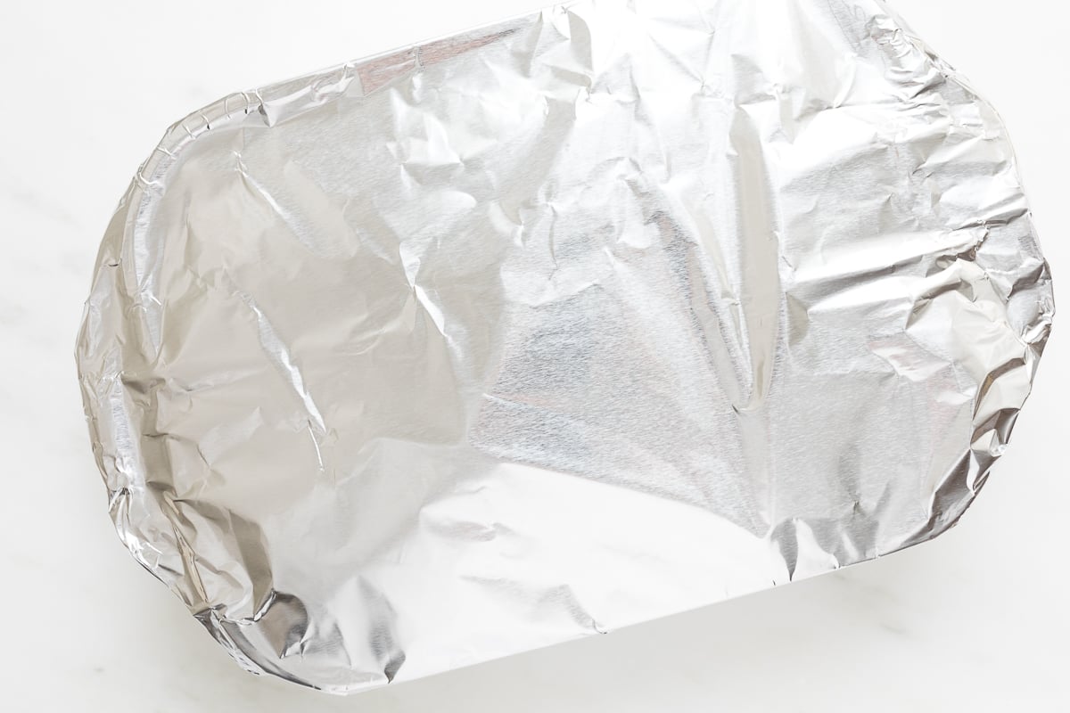 A piece of aluminum foil with a hot ham and cheese sandwich on a white surface.