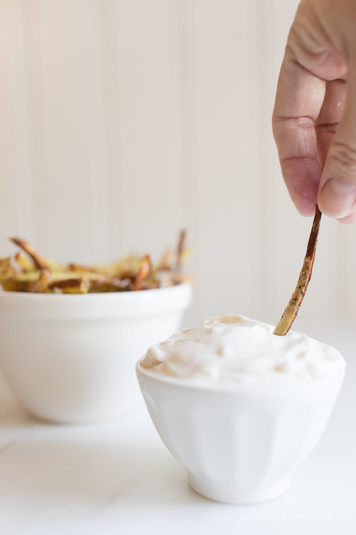 truffle aioli dip in a white bowl, hand reaching in with a french fry.