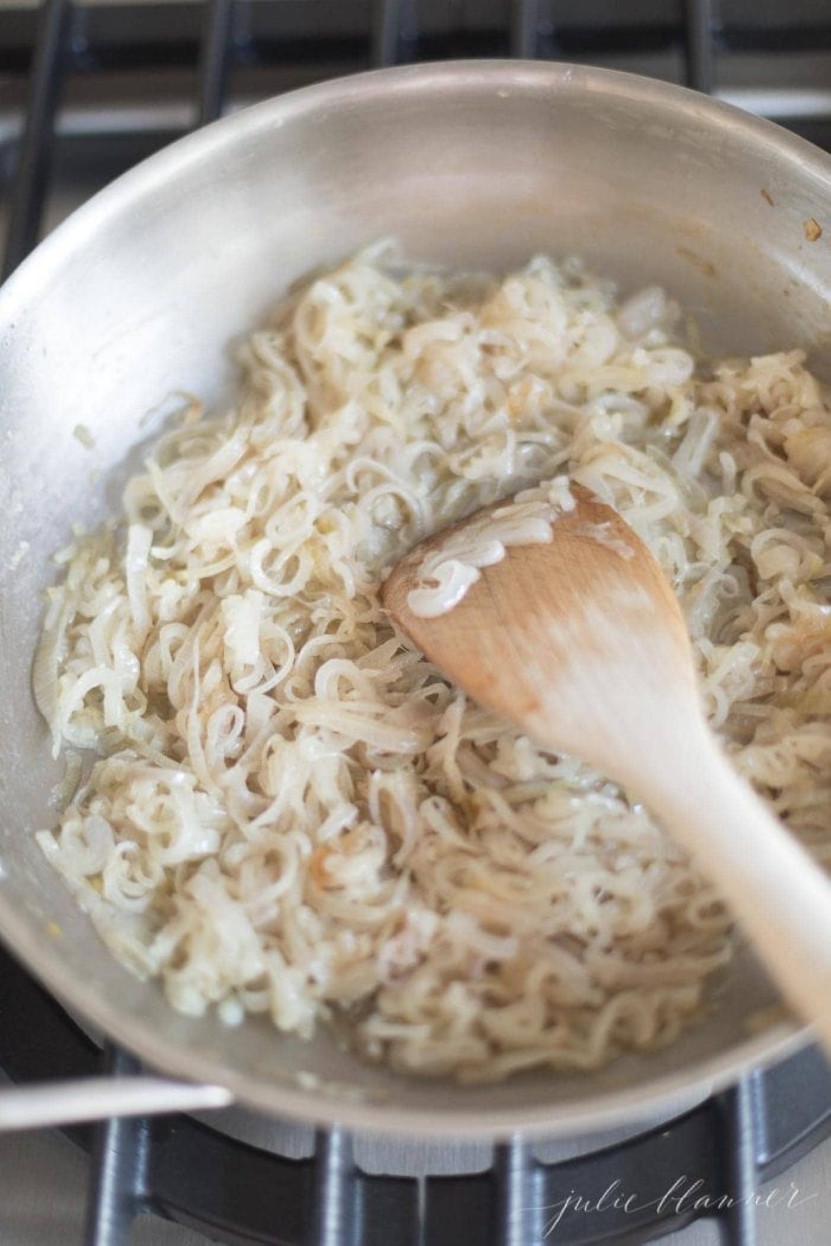 A silver pan on a stovetop, full of caramelized shallots