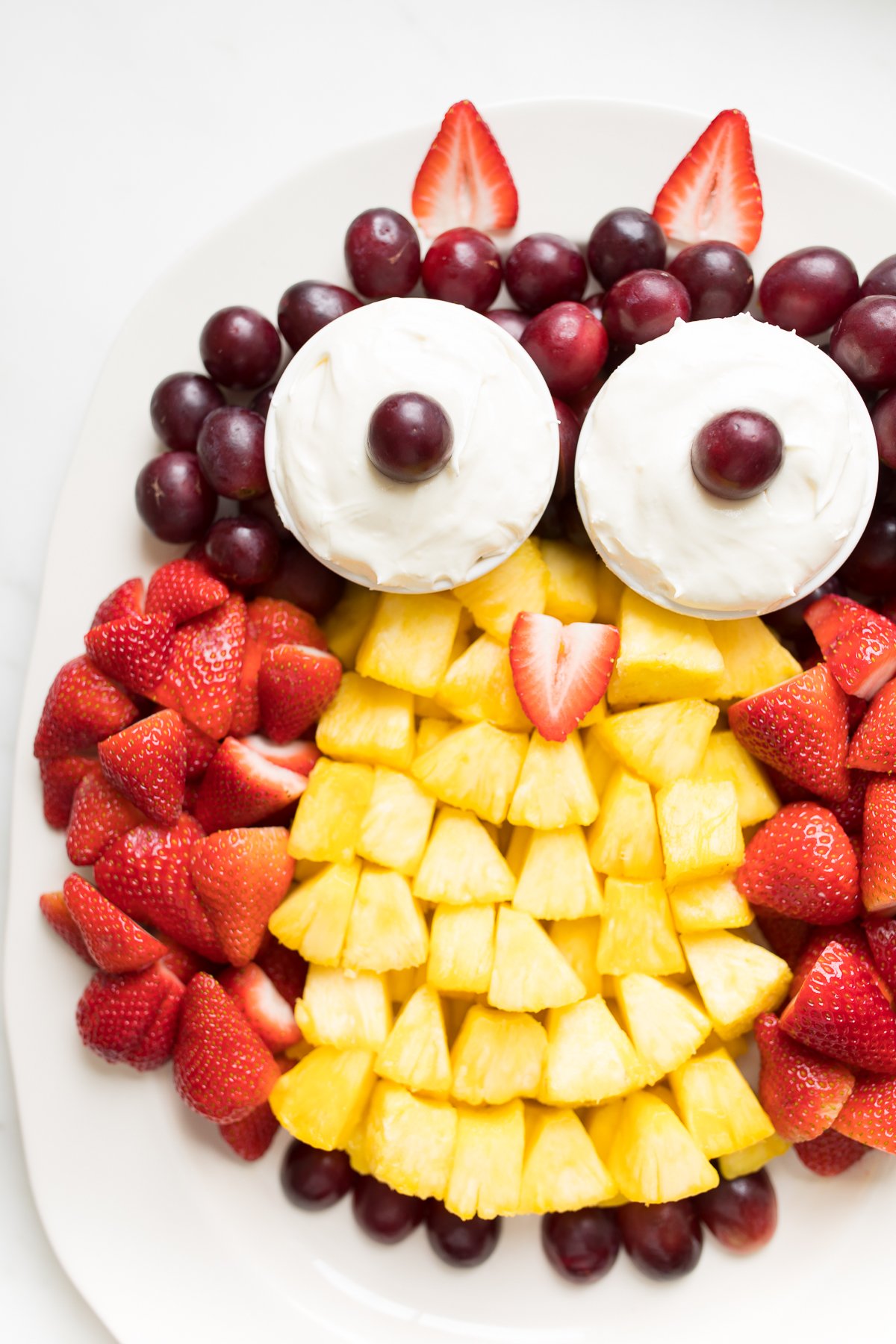 A fruit tray shaped into an owl, featuring cream cheese fruit dip as the owl's eyes.