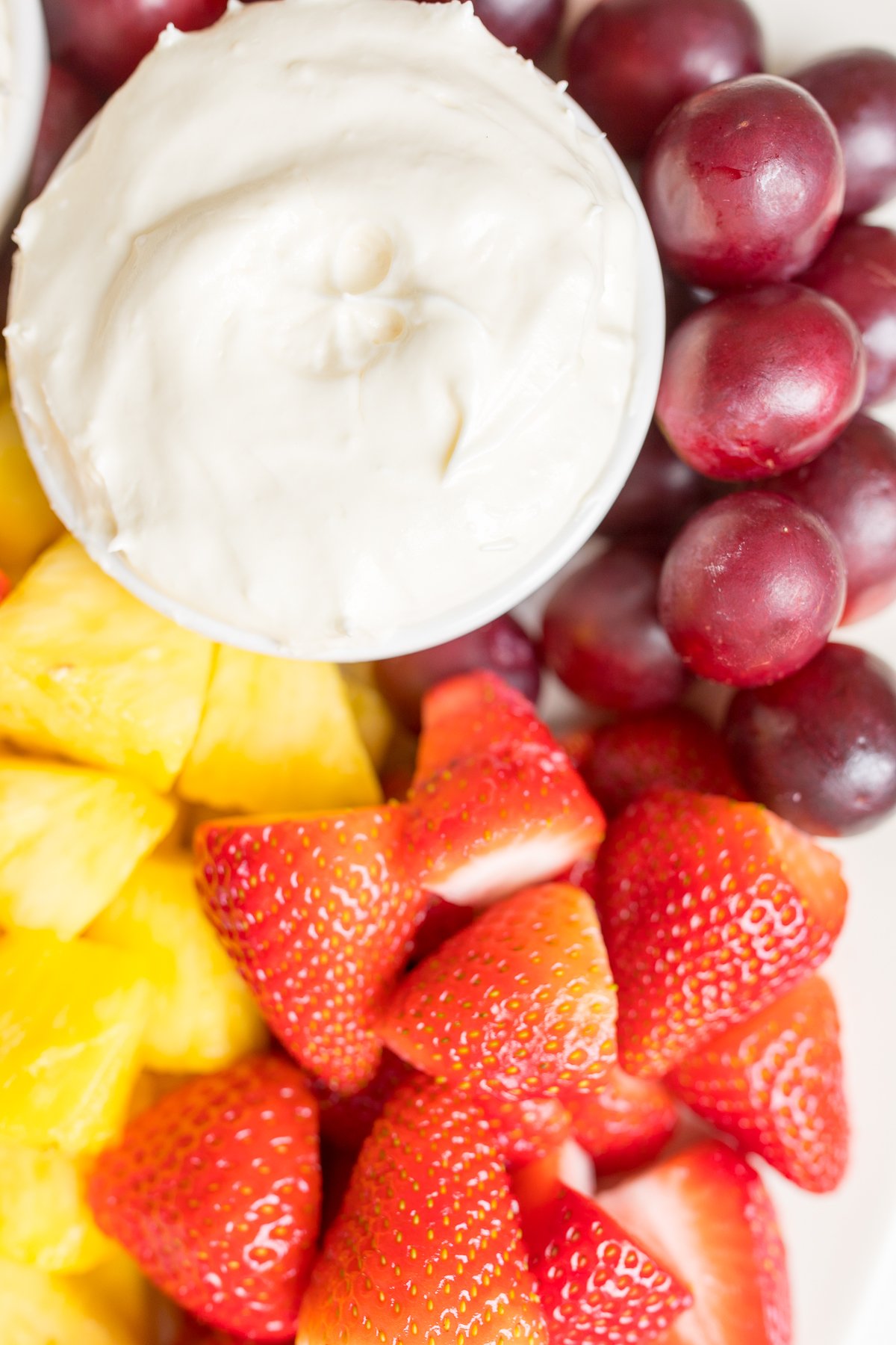 A white ceramic tray full of cut fruit and a small white bowl of cream cheese marshmallow fruit dip.