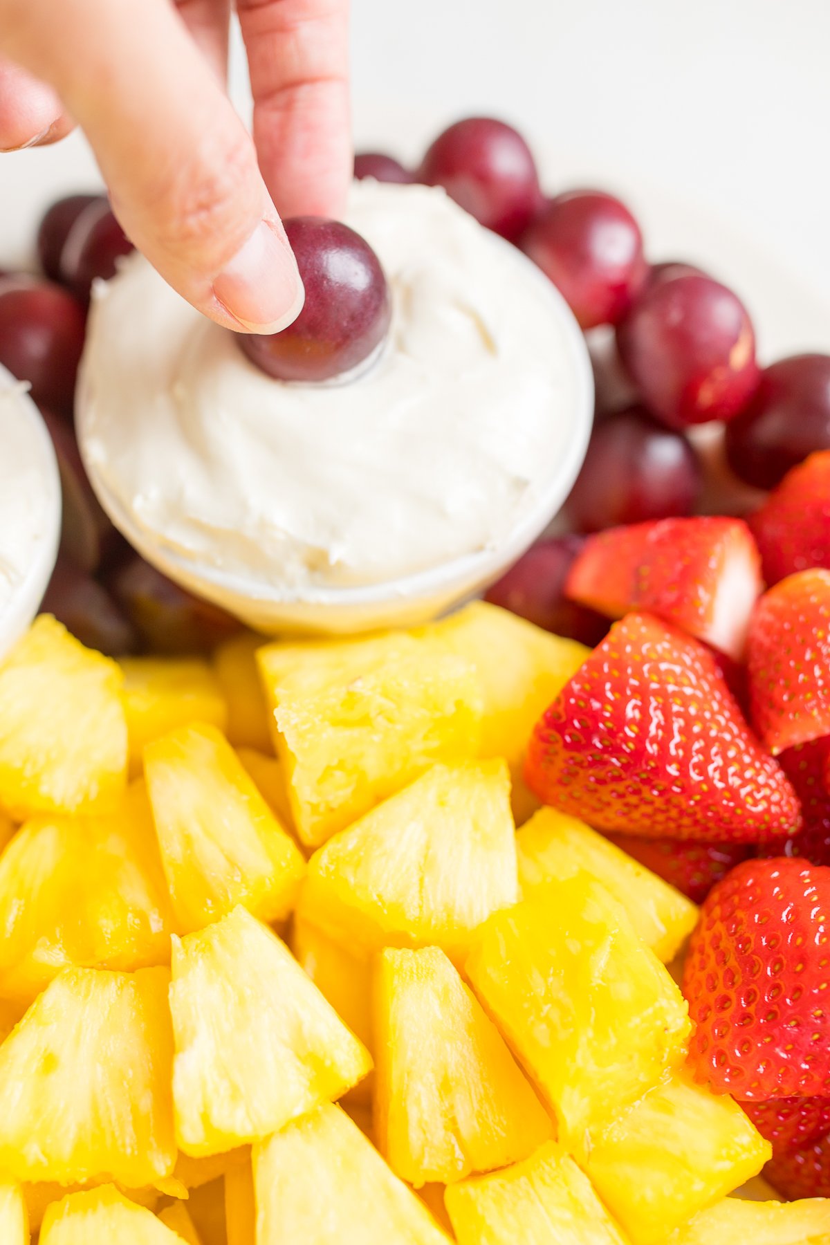 A white ceramic tray full of cut fruit and a small white bowl of cream cheese marshmallow fruit dip.