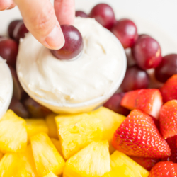 A white ceramic tray full of cut fruit and a small white bowl of cream cheese marshmallow fruit dip.