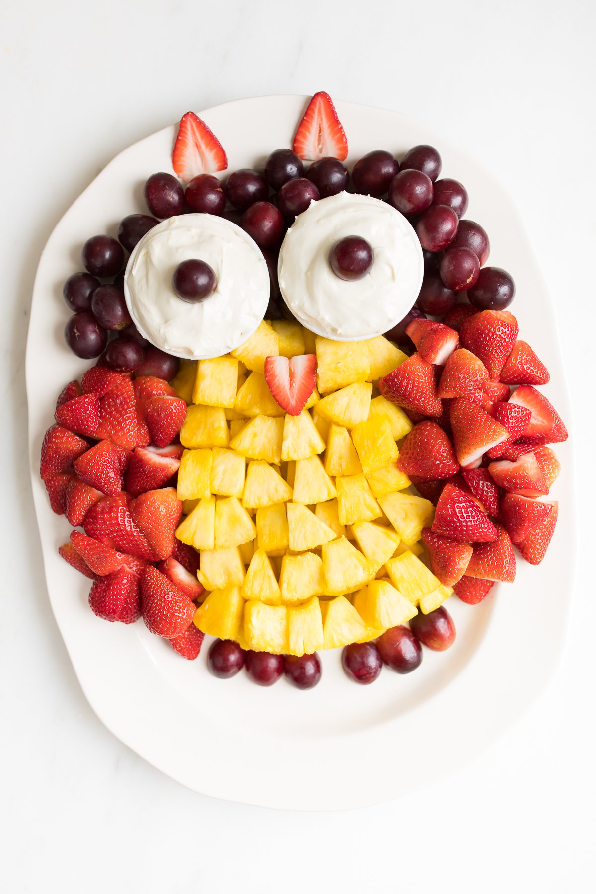 A fruit tray shaped into an owl, featuring cream cheese fruit dip as the owl's eyes.