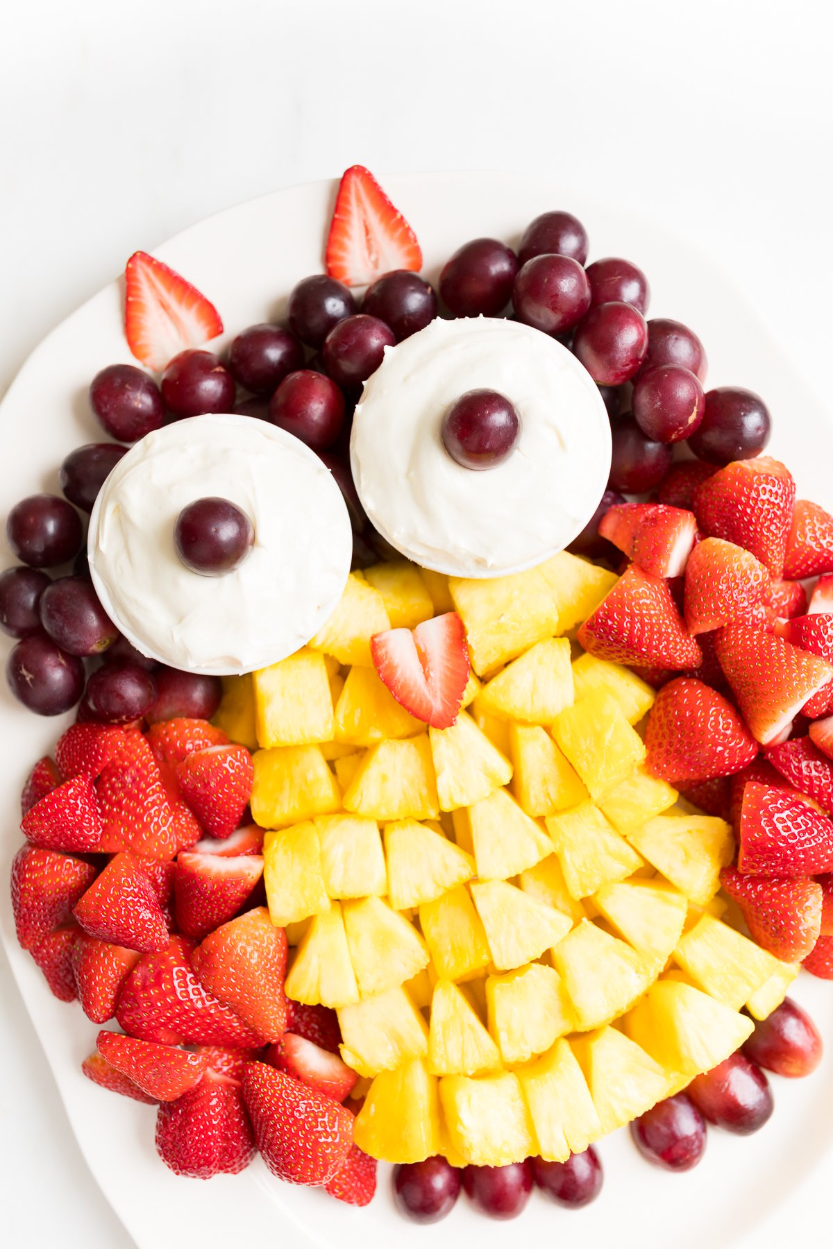 A fruit tray shaped into an owl, featuring cream cheese fruit dip as the owl's eyes.