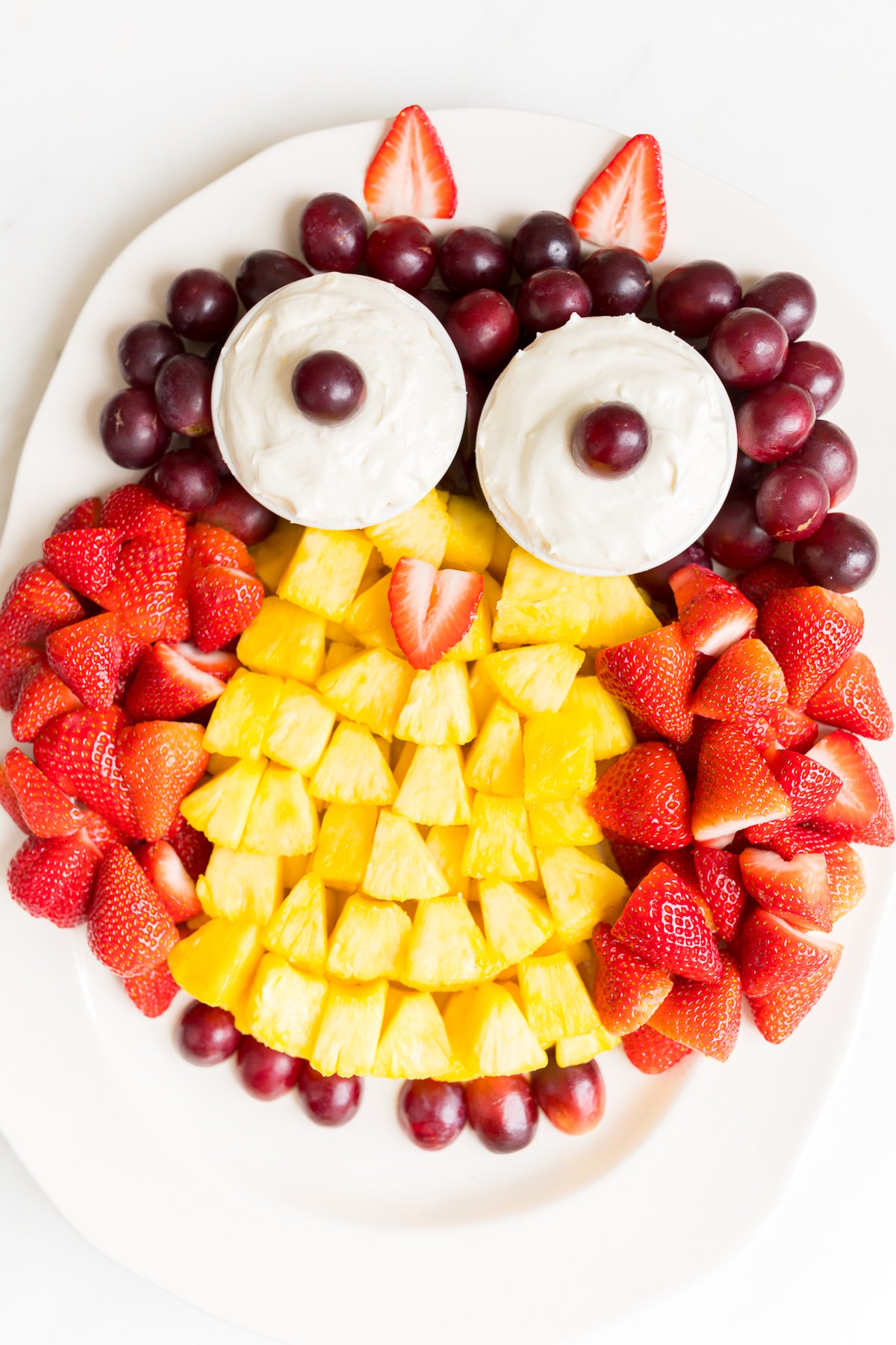 A fruit tray shaped into an owl, featuring cream cheese fruit dip as the owl's eyes.