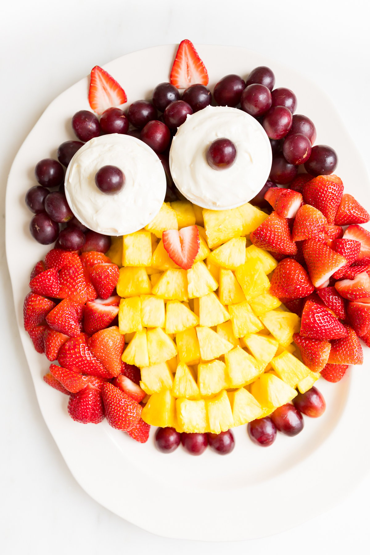 A fruit tray shaped into an owl, featuring cream cheese fruit dip as the owl's eyes.