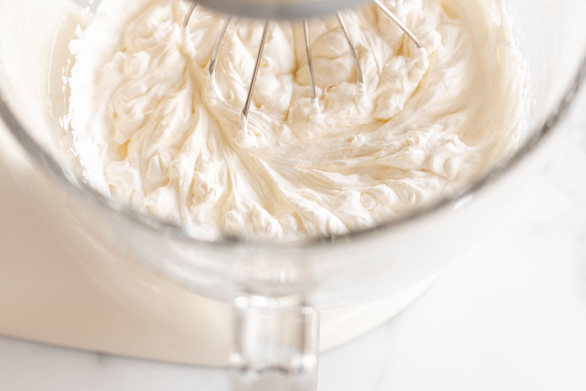 Whipped cream in the glass bowl of a stand mixer in a tutorial for how to make homemade whipped cream.