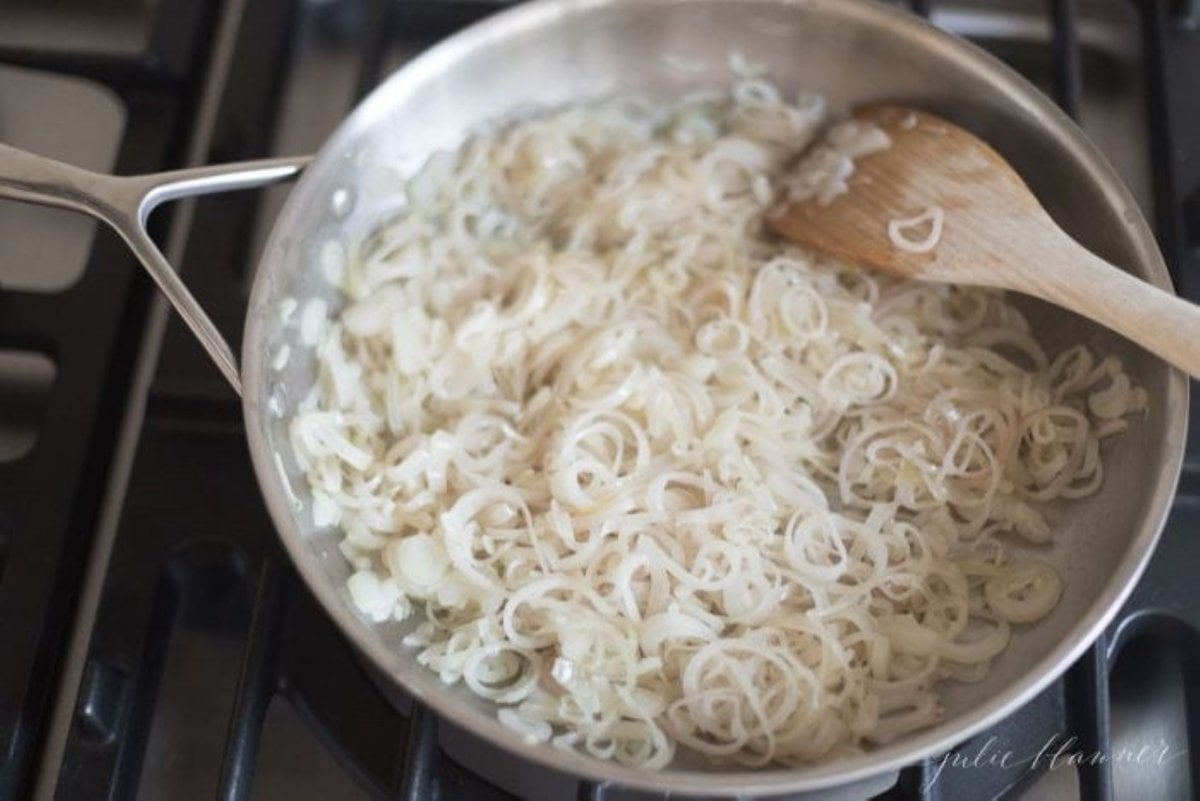 A silver pan on a stovetop, full of caramelized shallots