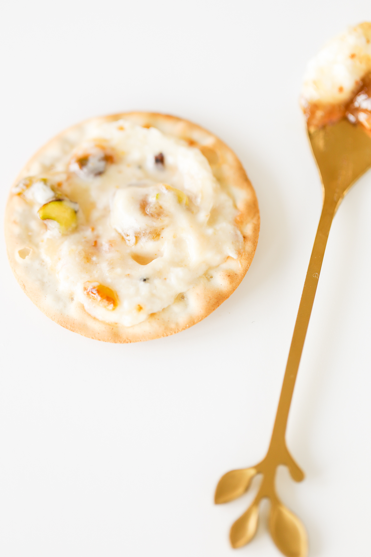 A cracker with goat cheese and pistachios on it.