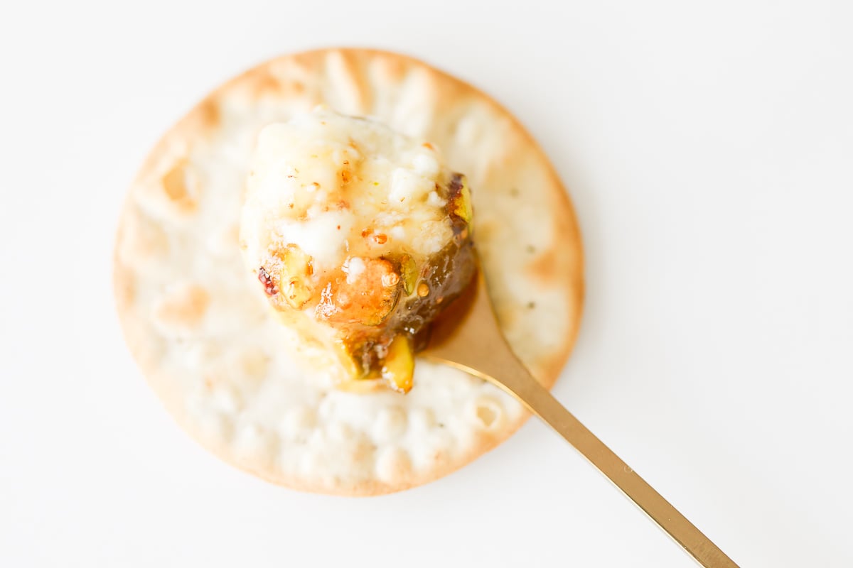 A cracker with goat cheese and pistachios on it.