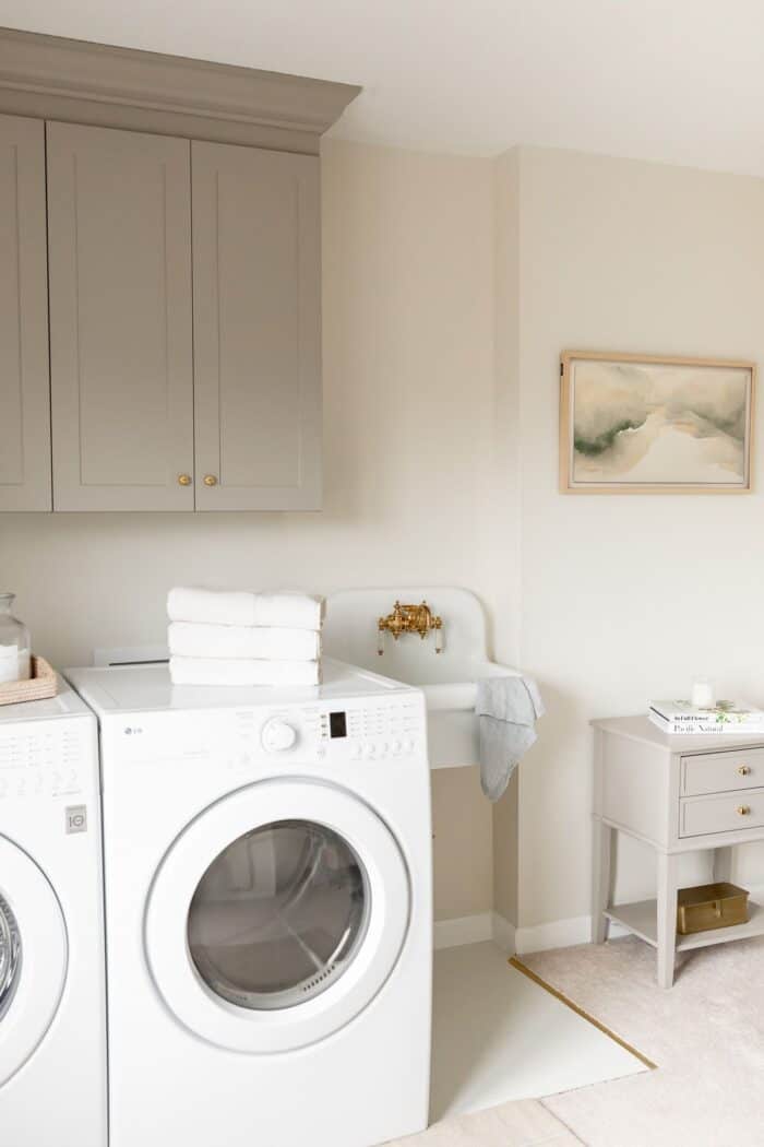 A laundry room with a small white sink and a side table and cabinets painted with furniture paint