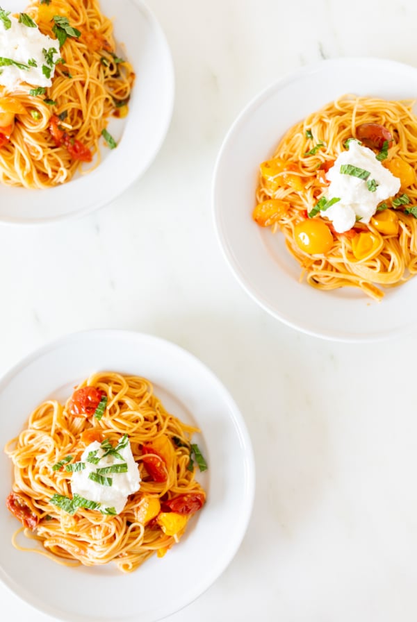 Small white plates on a marble countertop, with servings of cherry tomato pasta.