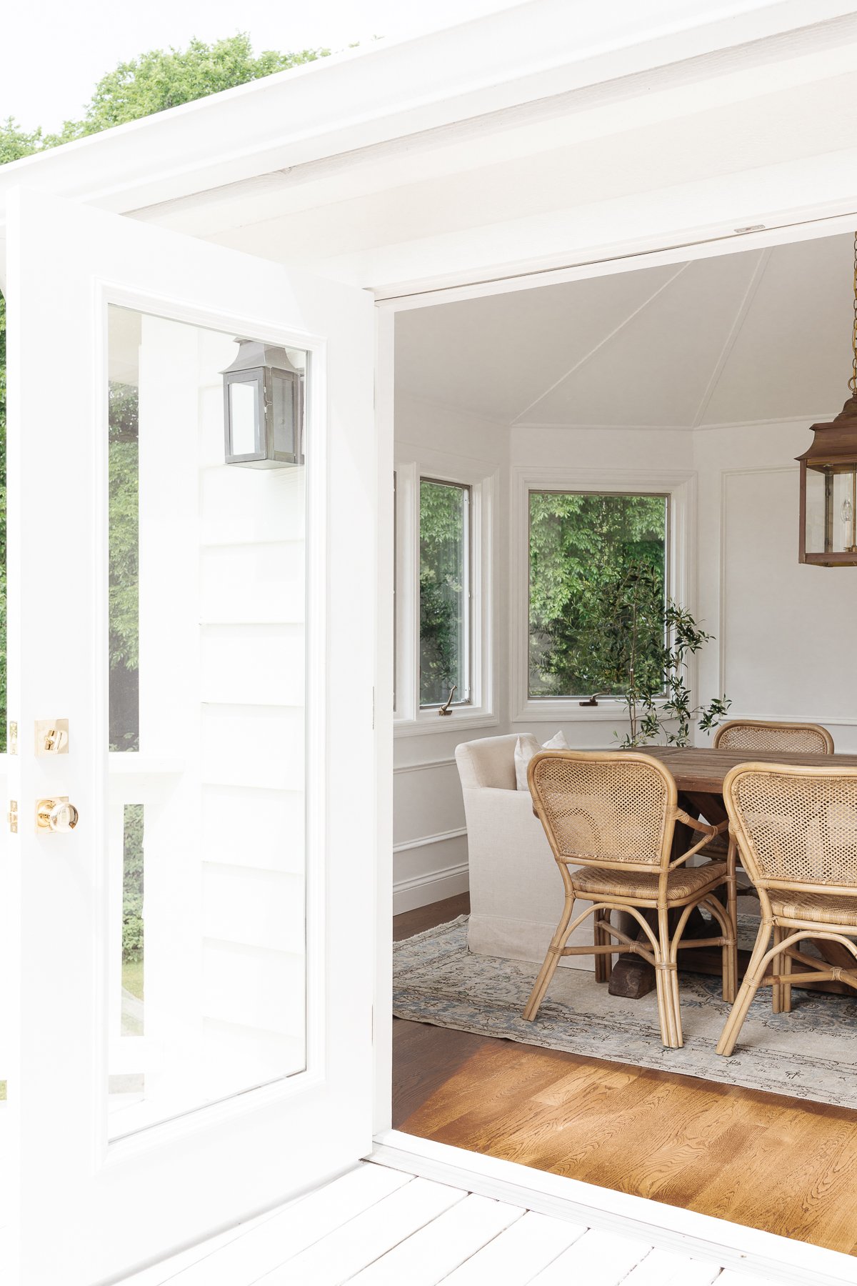 A white breakfast nook featuring a wooden table and rattan chairs with a brass lantern hanging above.