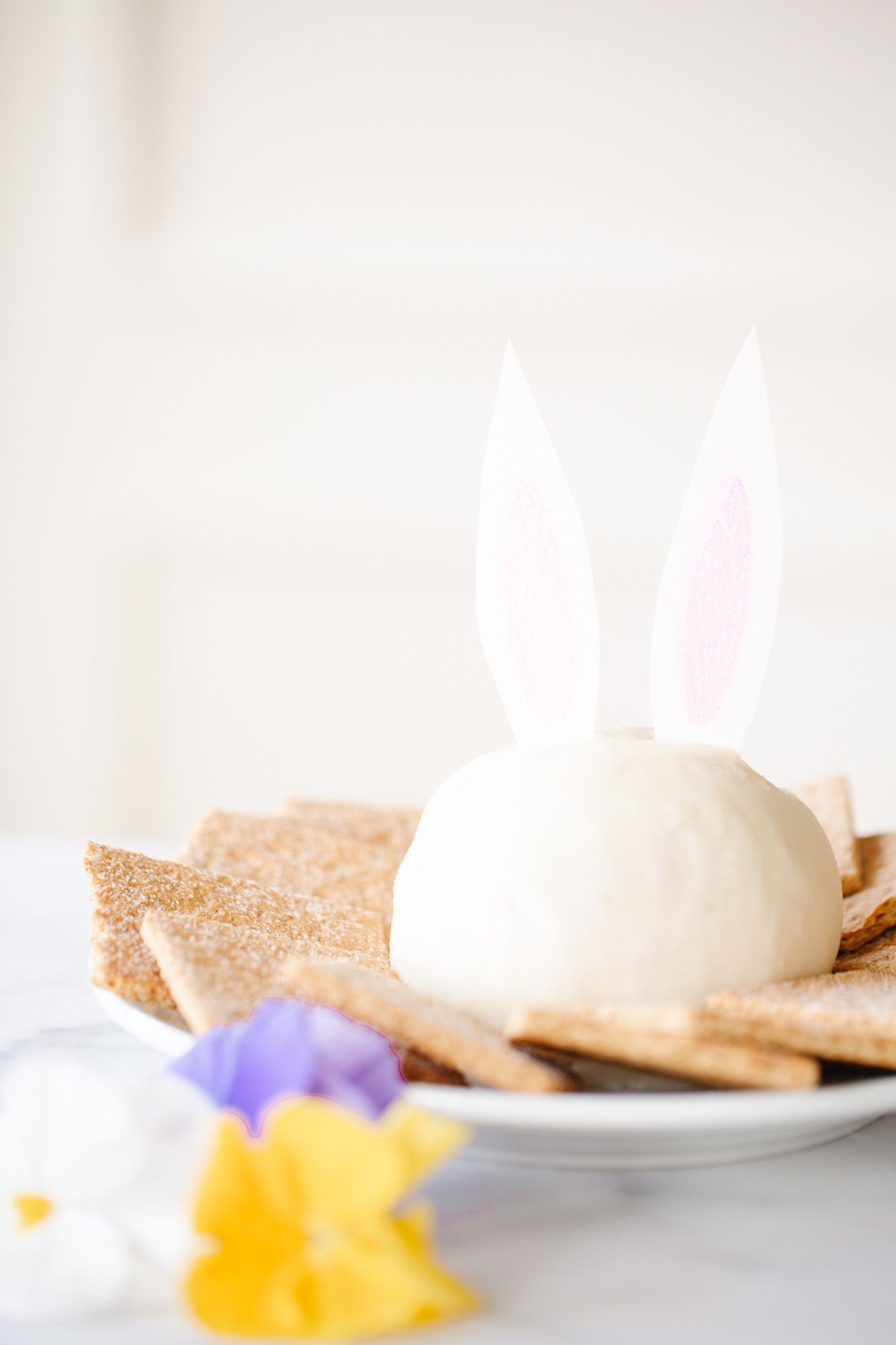 A white plate with an Easter Bunny cheese ball with paper ears, surrounded by graham crackers.