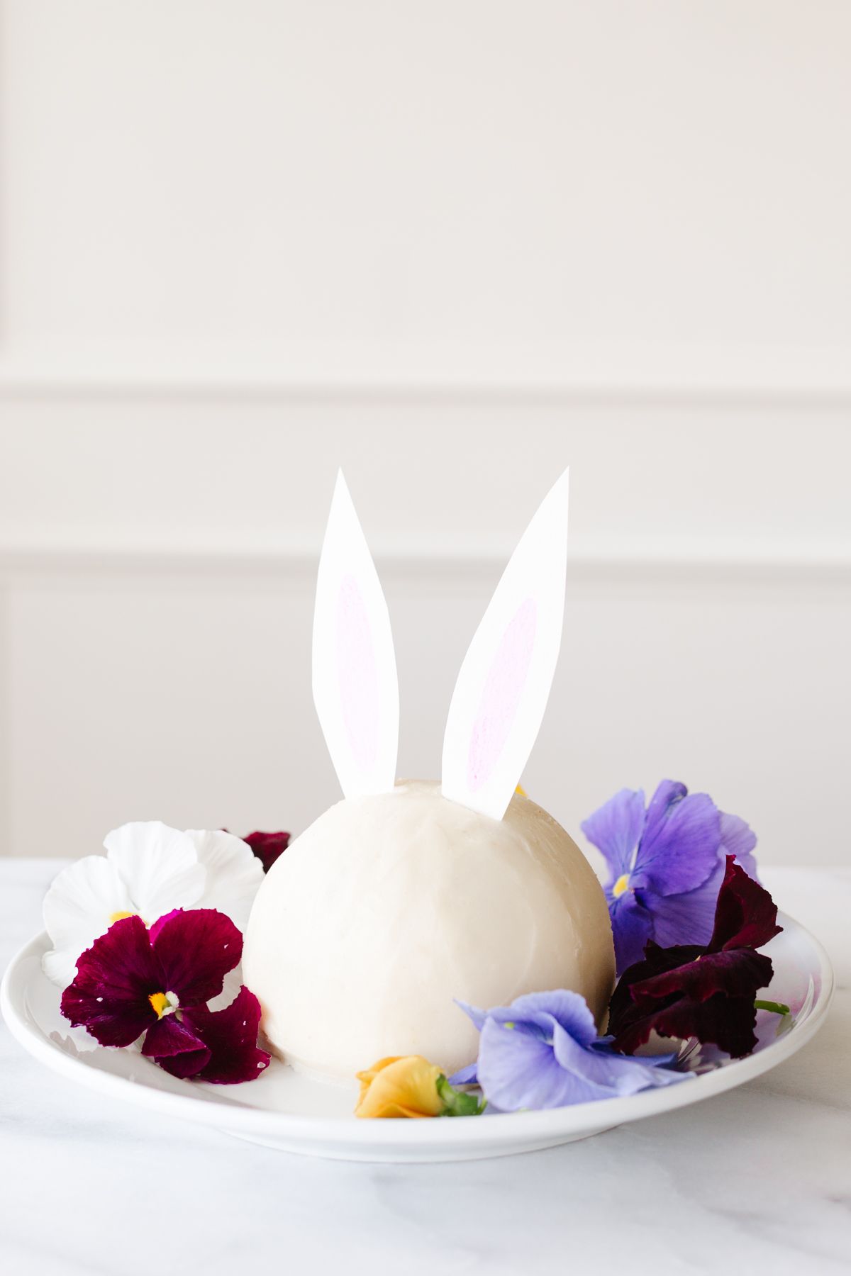 A white plate with an Easter bunny cheese ball surrounded by fresh flowers