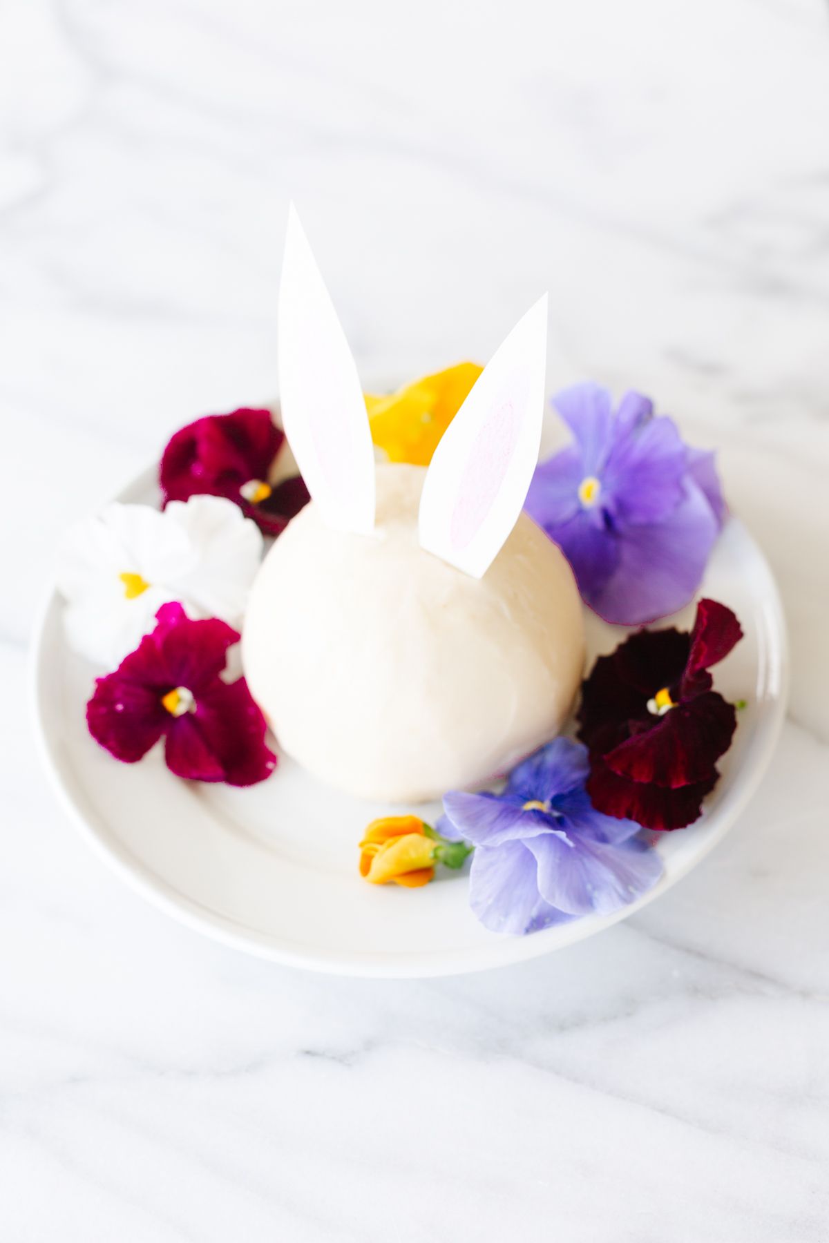 A white plate with an Easter bunny cheese ball surrounded by fresh flowers