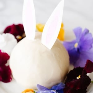 A white plate with an Easter bunny cheese ball surrounded by fresh flowers