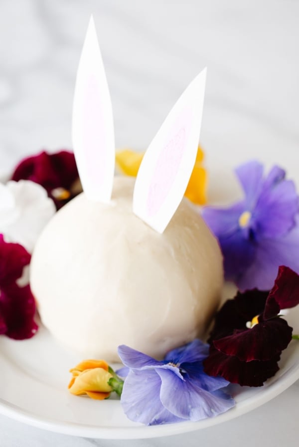 A white plate with an Easter bunny cheese ball surrounded by fresh flowers