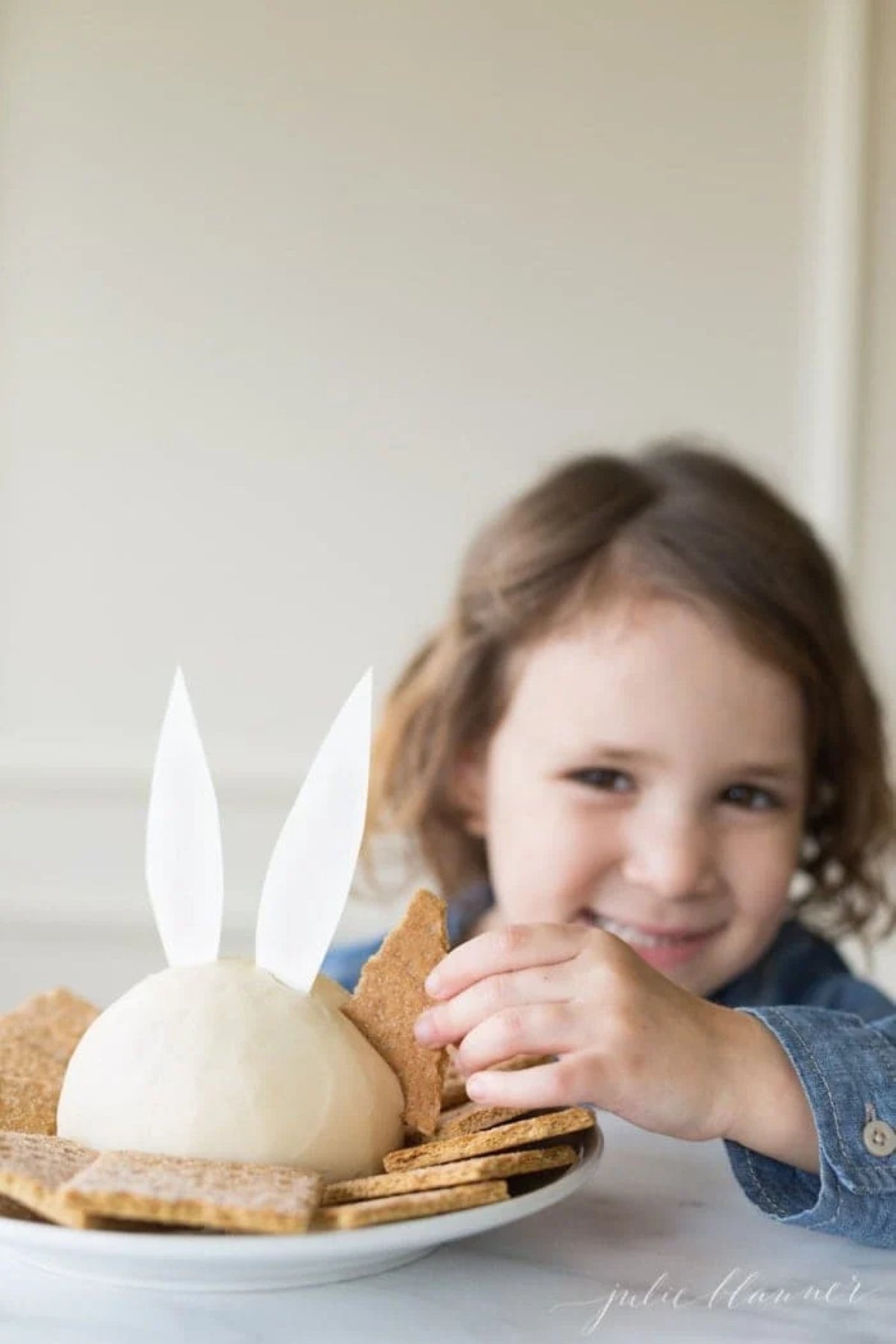 A little girl using a graham cracker to dip into an Easter bunny cheese ball.