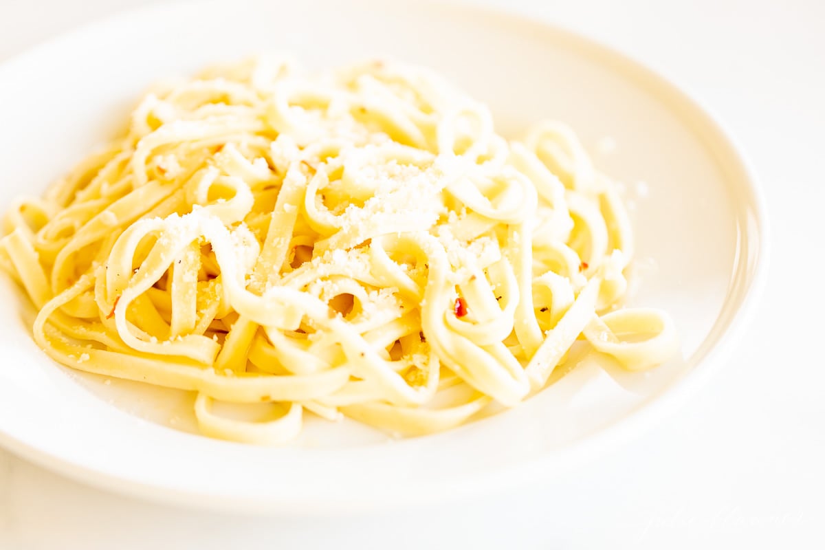 A white plate full of pasta in a white wine sauce. 