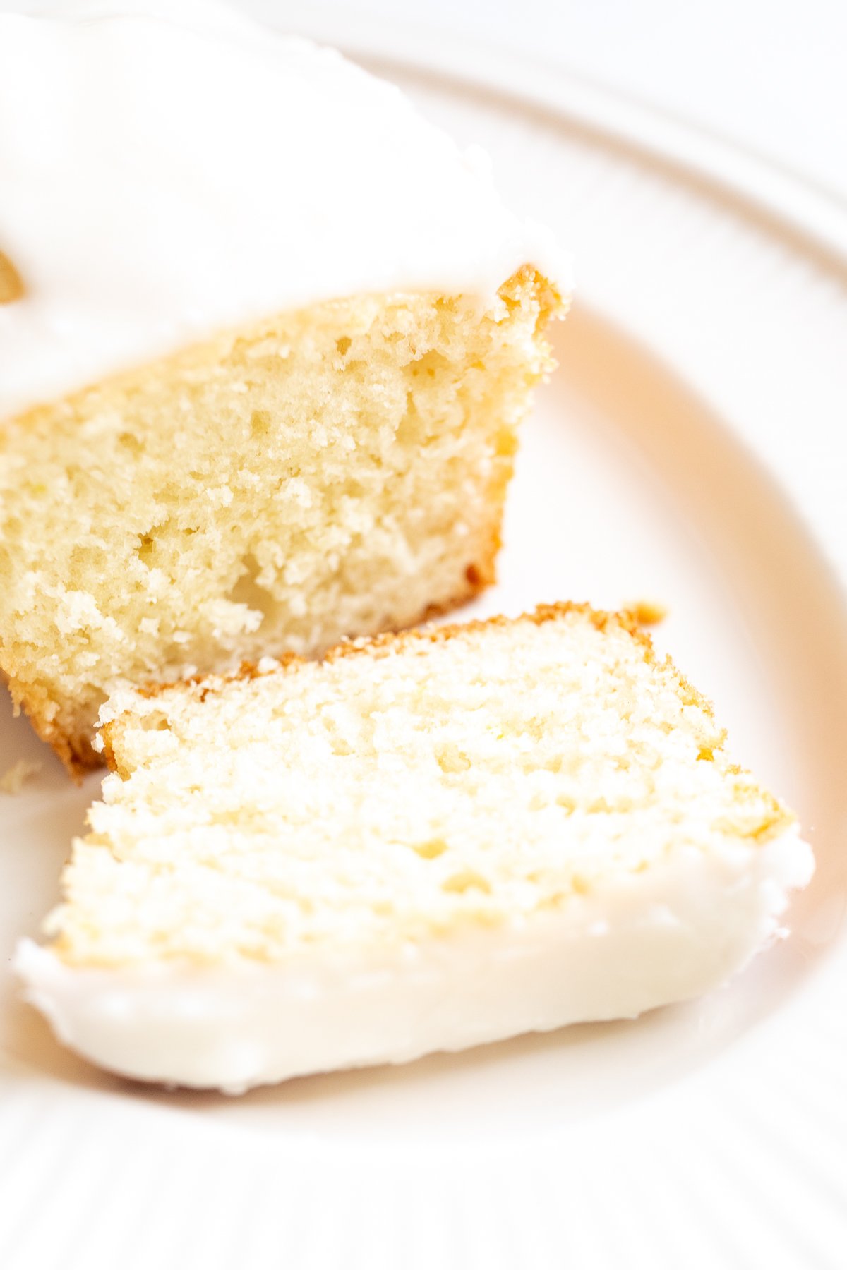 A frosted lemon loaf on a white platter, one slice cut.