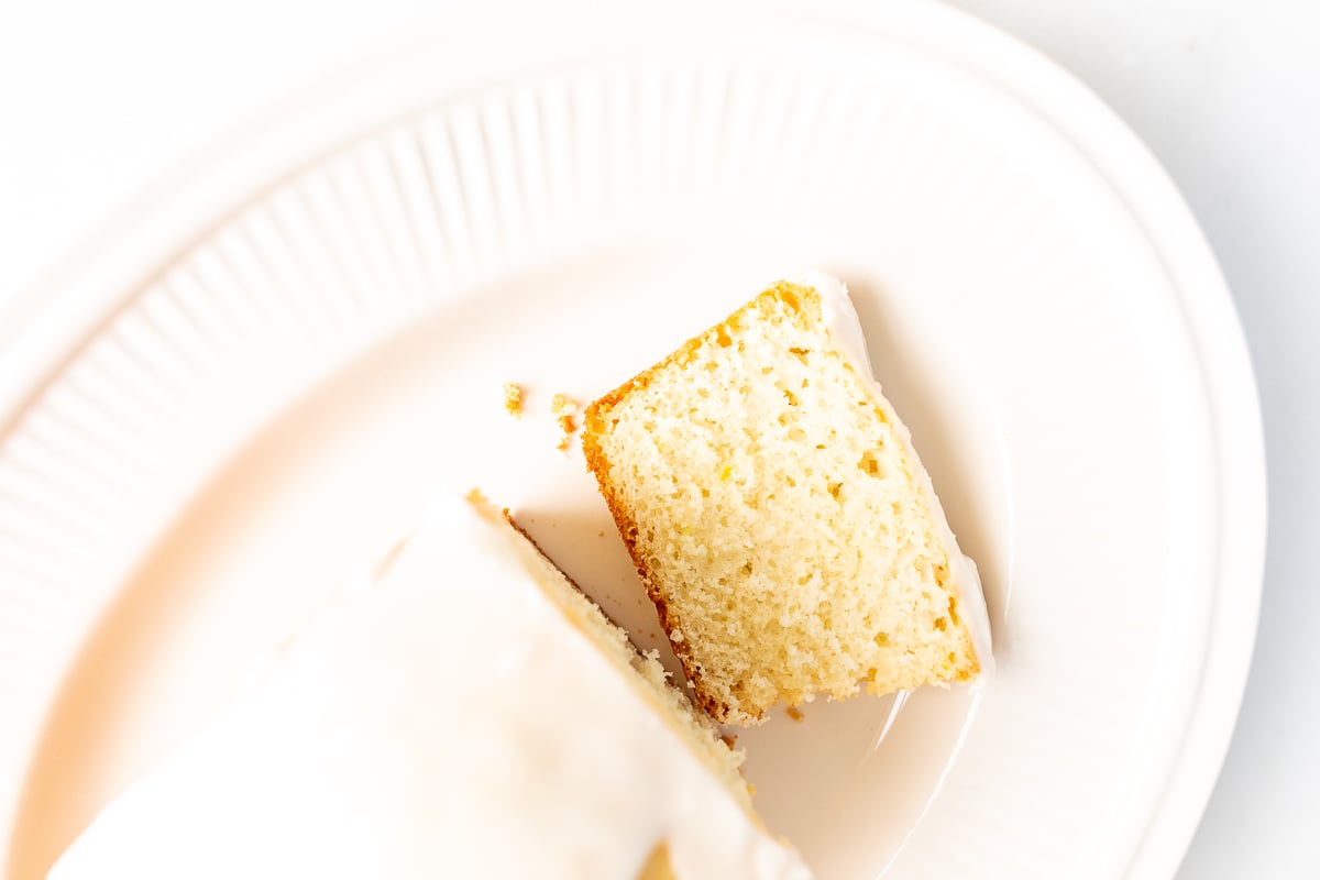 A frosted lemon loaf on a white platter, one slice cut.