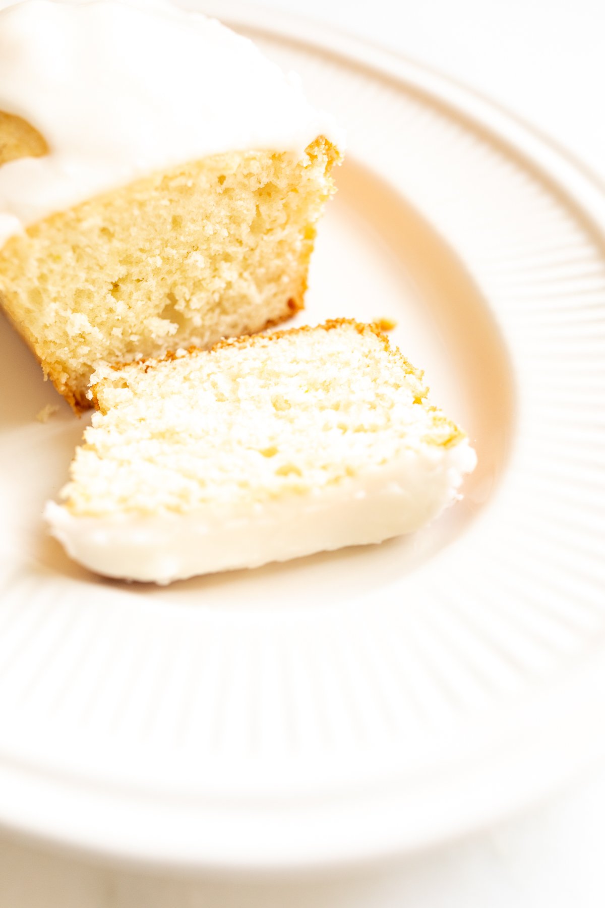 A frosted lemon loaf on a white platter, one slice cut.