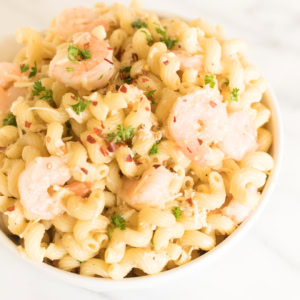 A white bowl of seafood pasta salad on a marble surface.