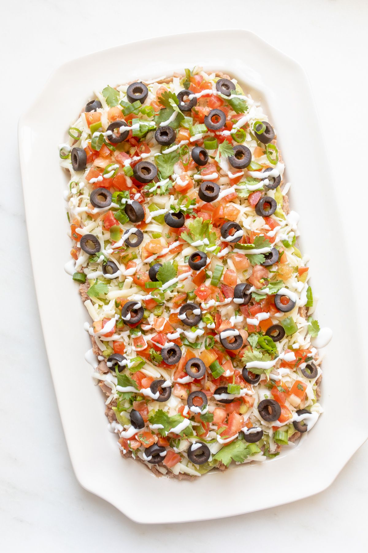 A hand adding garnish to a white platter of 7 layer dip.