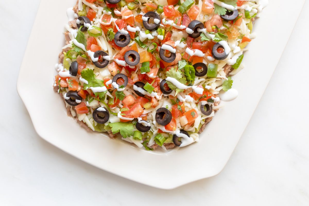 A white platter full of seven layer dip.