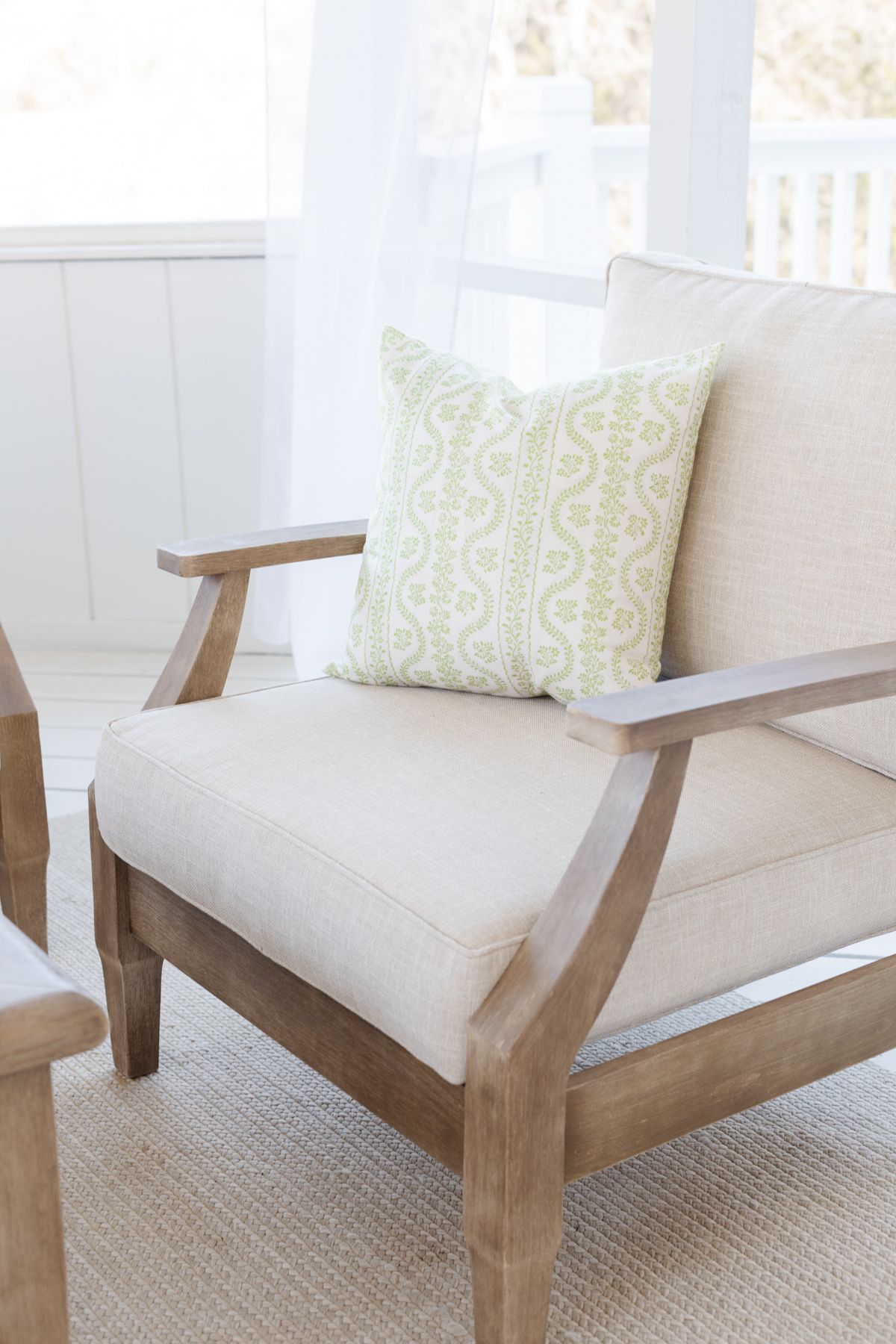 An outdoor wood patio chair with beige cushions and a green striped Amazon pillow cover.