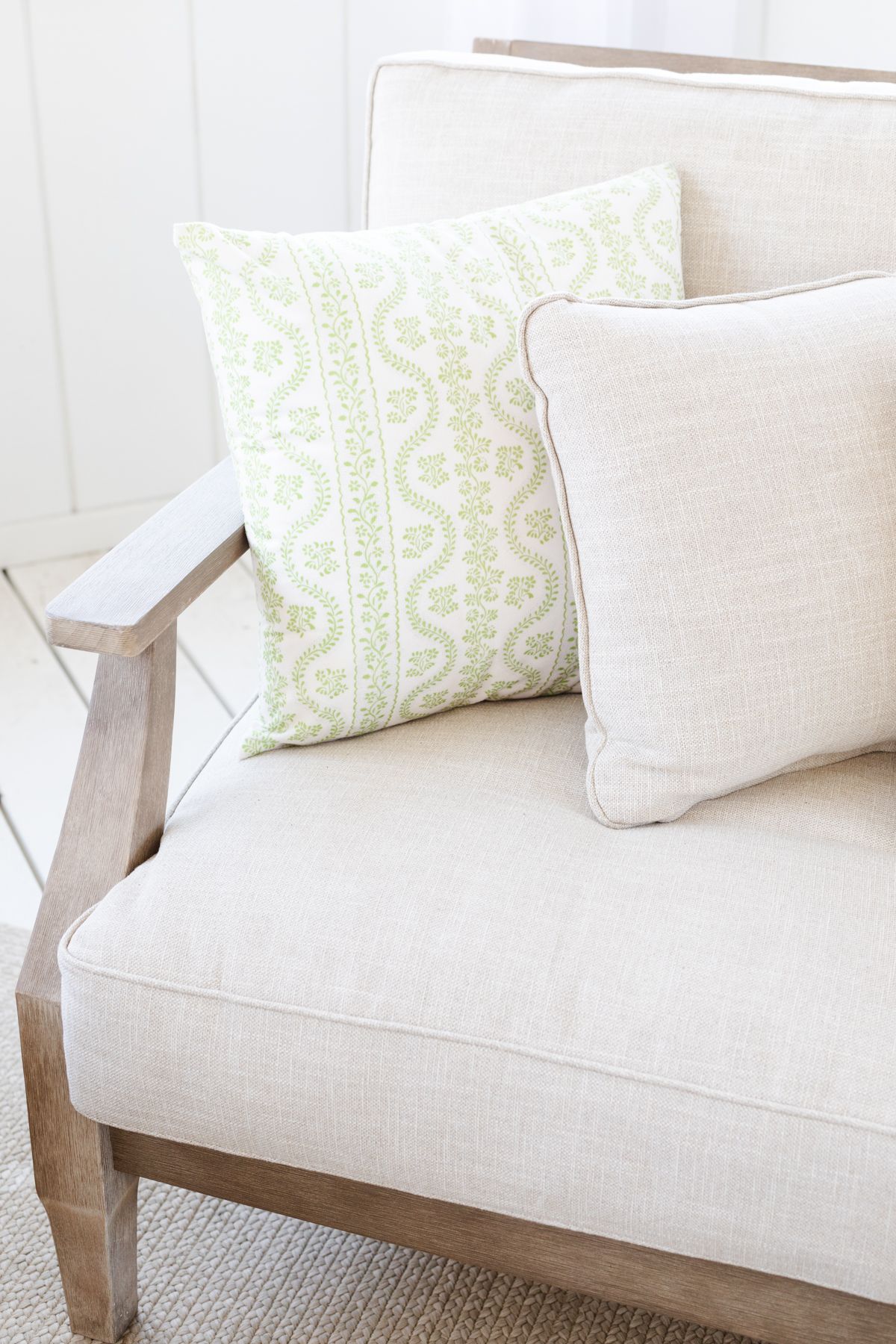 An outdoor wood patio chair with beige cushions and a green striped Amazon pillow cover.