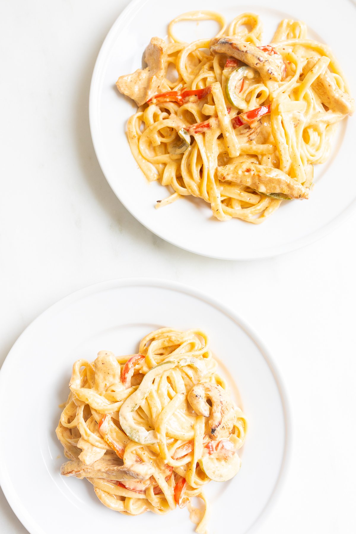 Two white plates of cajun chicken pasta.