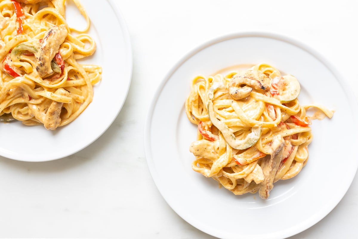 Two white plates of cajun chicken pasta.