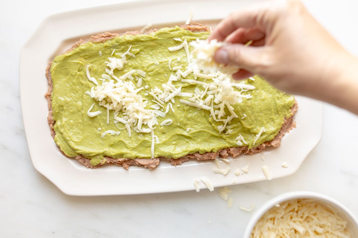 A white platter layered with beans and guacamole for a 7 layer dip recipe.