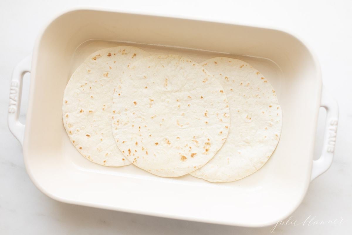 A Mexican breakfast casserole being put together in a white baking dish