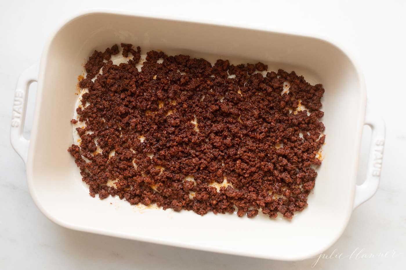 A Mexican breakfast casserole being put together in a white baking dish