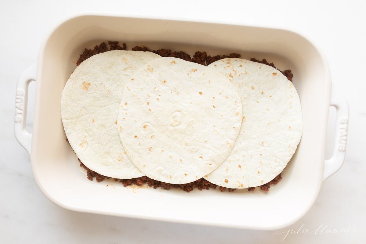 A Mexican breakfast casserole being put together in a white baking dish