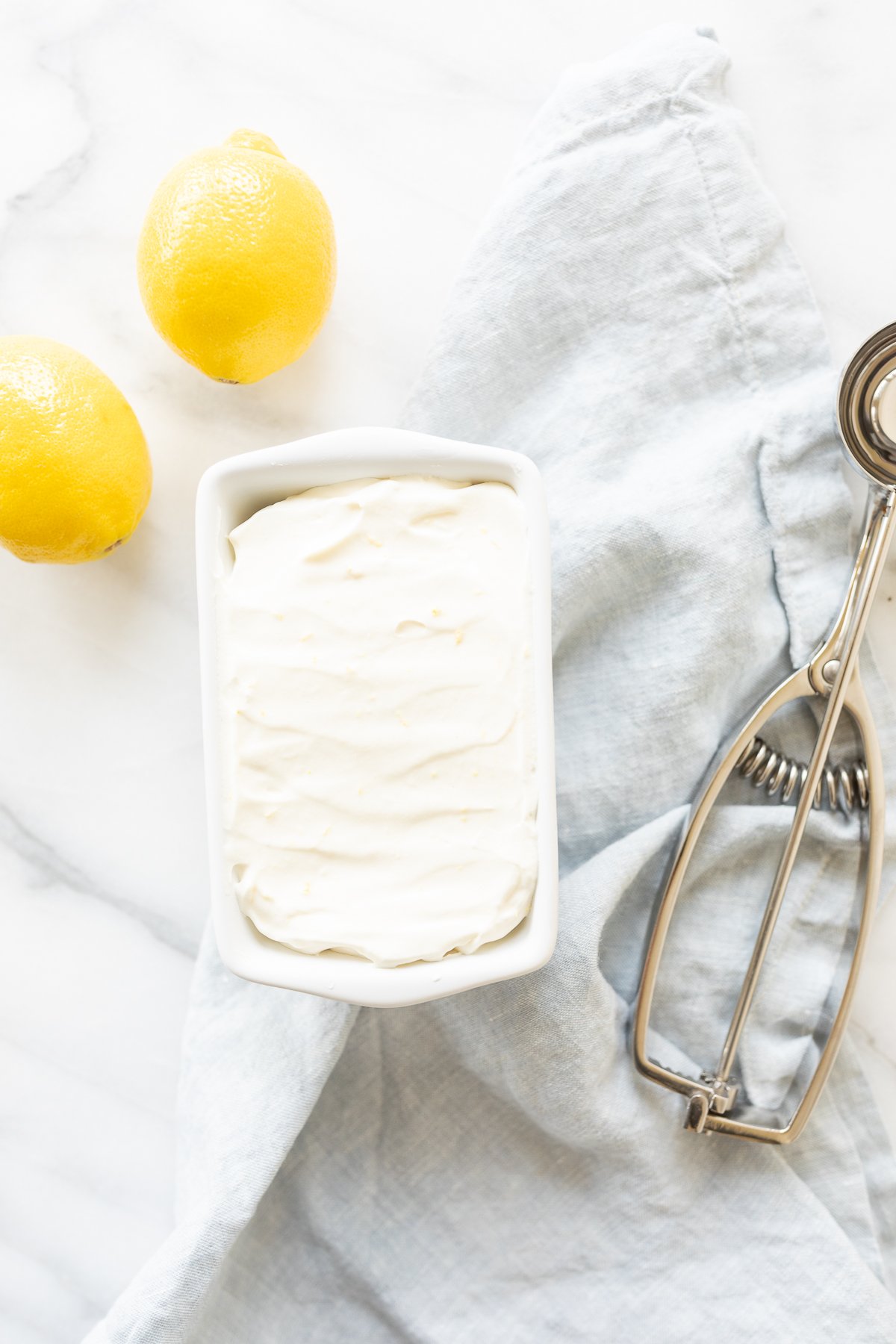 Lemon ice cream in a ceramic mini loaf pan, with fresh lemons to the side.