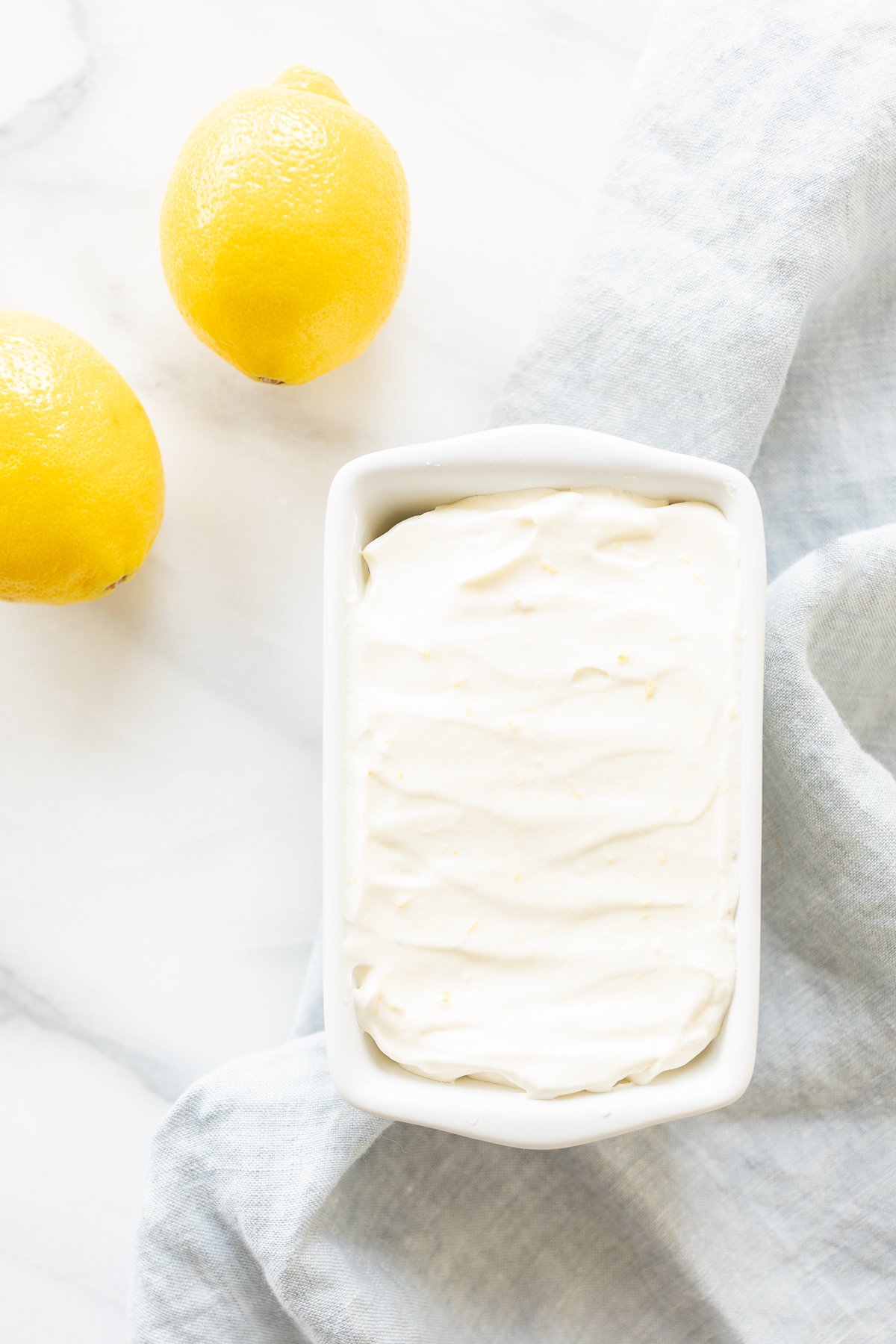 No churn lemon ice cream in a ceramic mini loaf pan, with fresh lemons to the side.