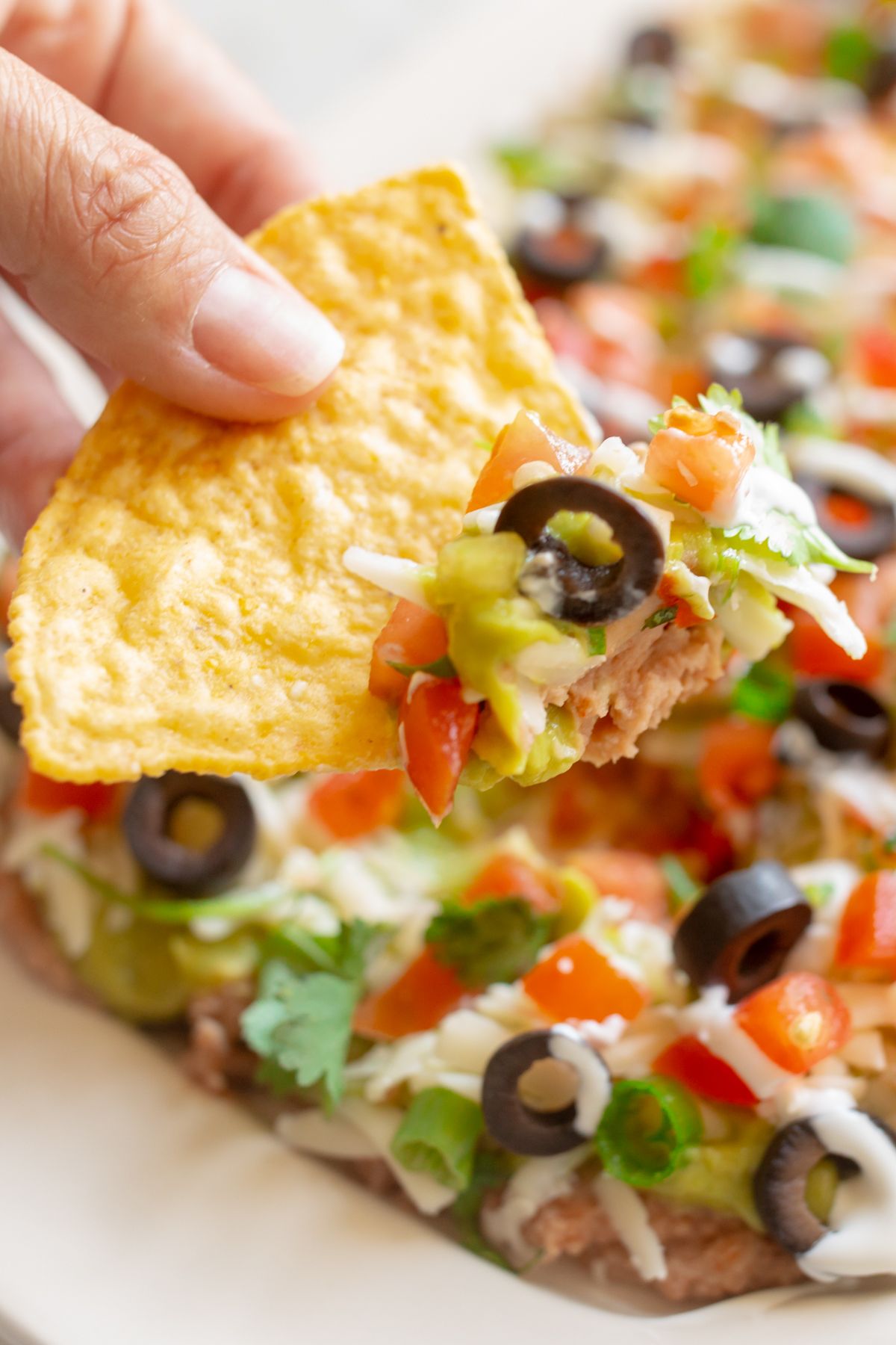 A hand dipping a tortilla chip into a platter of 7 layer dip.