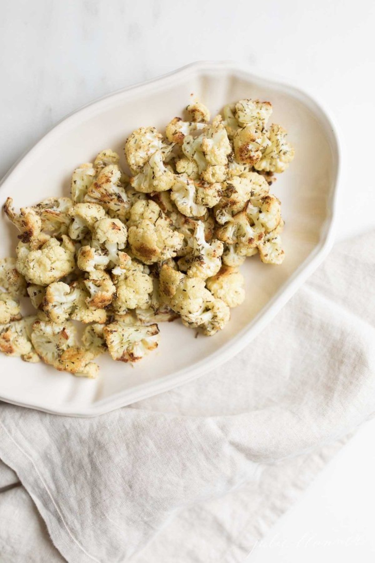 An oval white platter, filled with roasted cauliflower that is crispy and browned at the edges.