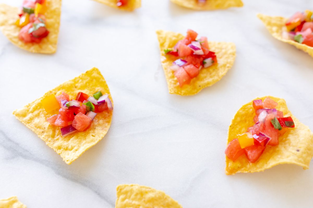 A marble countertop with tortilla chips scattered across, topped with fresh watermelon salsa.