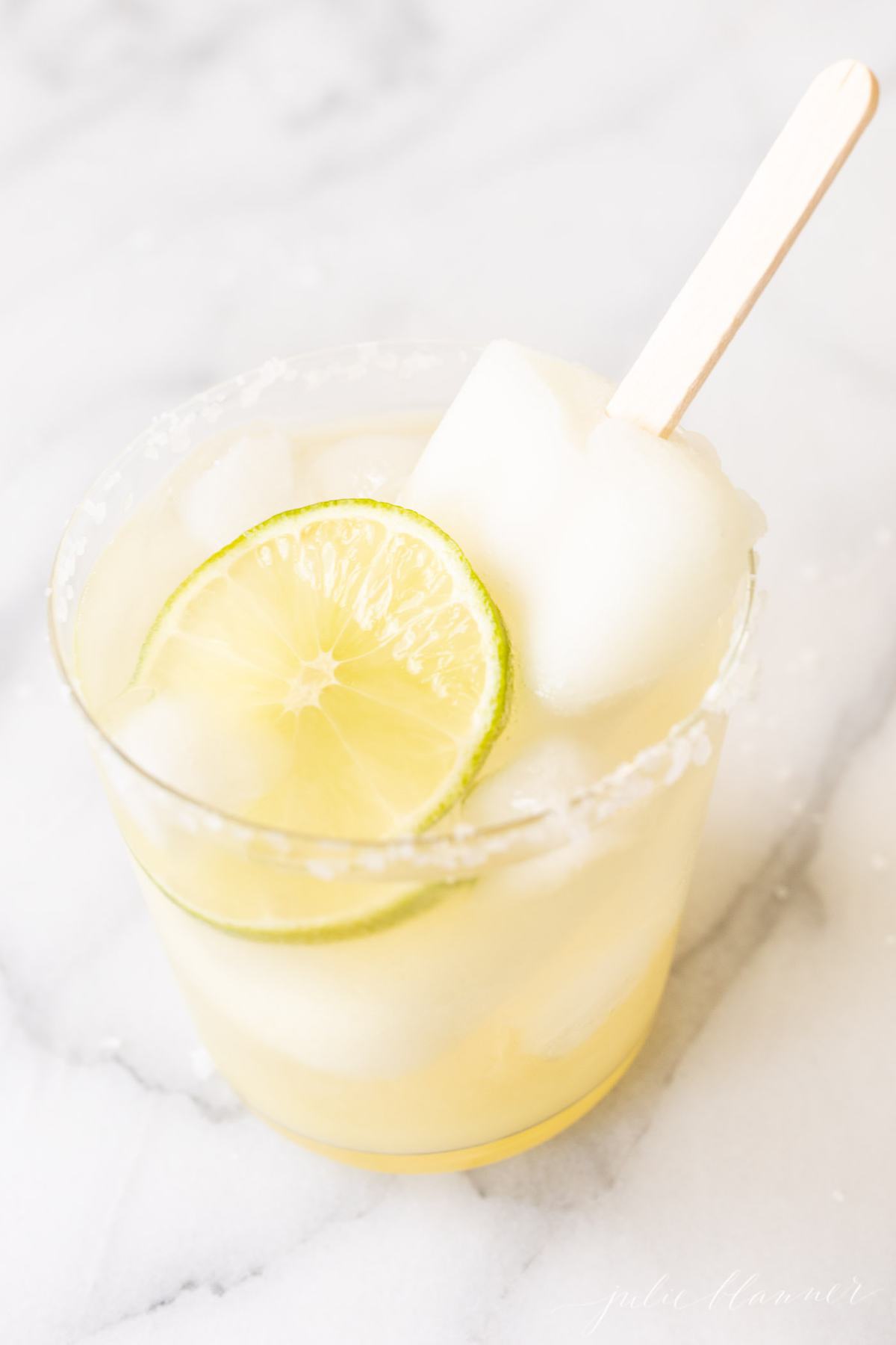 A Lime Popsicle Margarita in a glass on a marble surface.