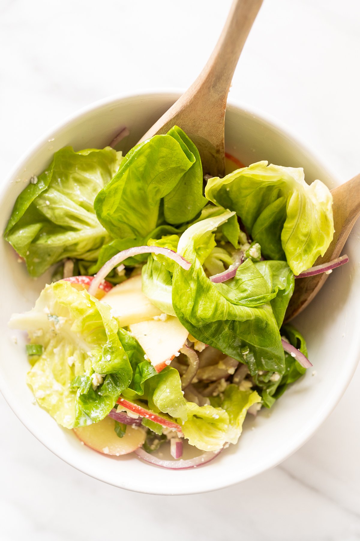 A white bowl full of homemade apple salad, with wooden serving spoons.