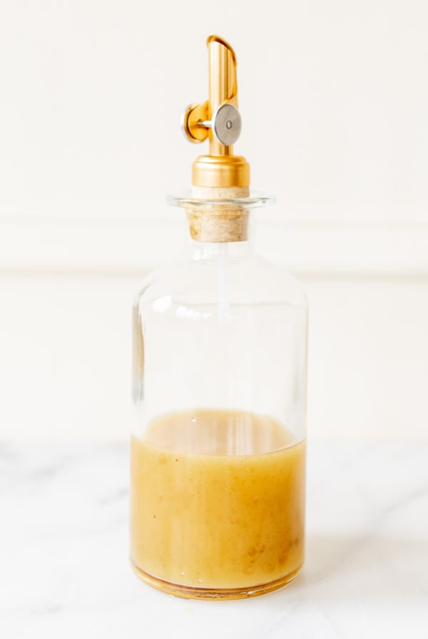 A glass bottle with a gold spout, full of pasta salad dressing.