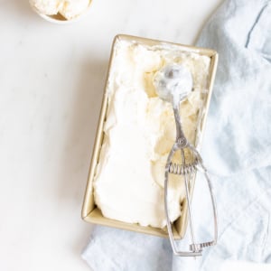 cream cheese ice cream in a loaf pan with an ice cream scooper and small white bowl of ice cream