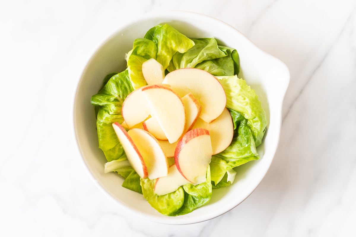 A bottle of dressing being poured over a salad in a white bowl.