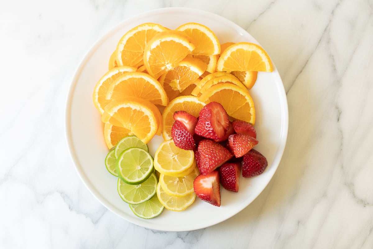 A white plate of sliced fruits for Spanish sangria.